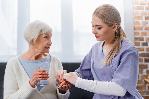 young nurse giving pills to elderly woman holding glass of water