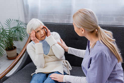 aged woman, suffering from memory loss, looking at social worker touching her on sofa