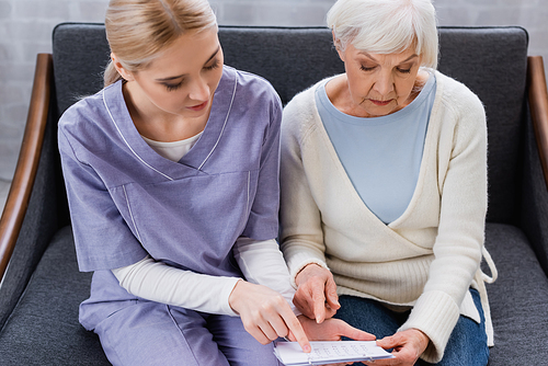 young nurse and senior woman, suffering from memory loss, pointing at calendar while sitting on couch
