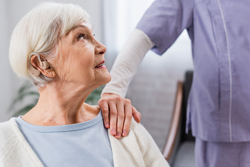 elderly woman with hearing aid looking at social worker touching her shoulder
