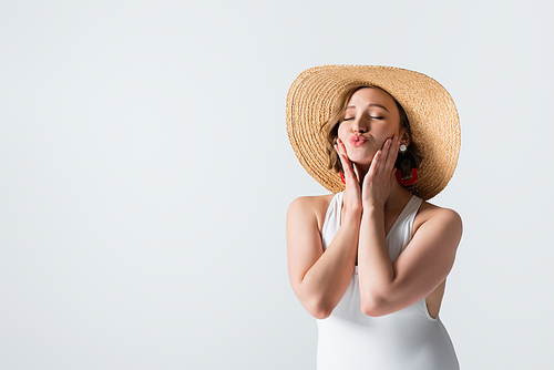 overweight young woman in earrings, swimsuit and straw hat pouting lips isolated on white