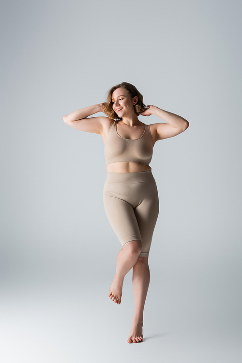 full length of happy overweight woman in underwear posing on grey