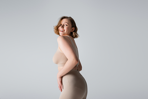 smiling overweight young woman in underwear posing isolated on grey