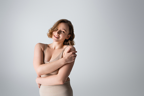 smiling overweight young woman in underwear posing on grey