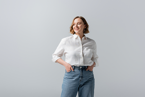 smiling overweight young woman in jeans posing with hands in pockets isolated on grey