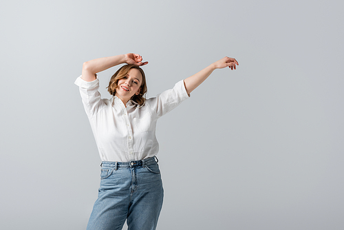 overweight and pleased woman in white shirt posing with hands above head isolated on grey