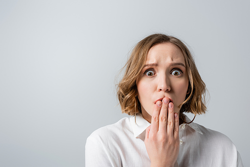 surprised overweight woman in white shirt covering mouth isolated on grey