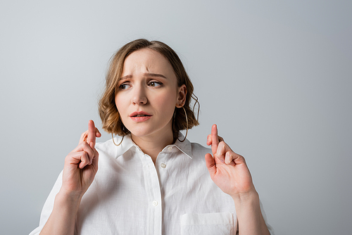 young overweight woman in white shirt with crossed fingers isolated on grey