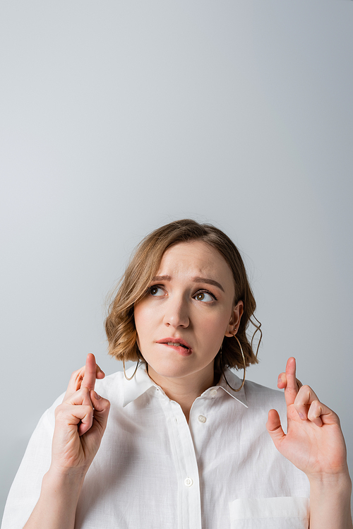 overweight woman in white shirt with crossed fingers isolated on grey