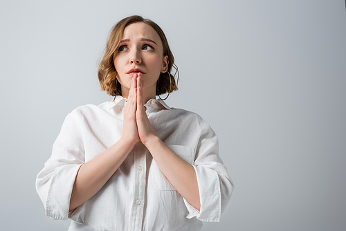 young overweight woman in white shirt with praying hands isolated on grey