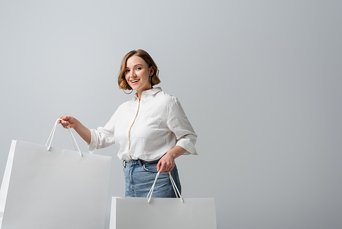 happy overweight woman in jeans and white shirt holding shopping bags isolated on grey