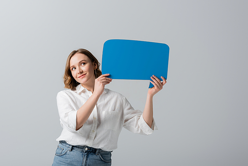 pleased overweight woman in white shirt holding blue speech bubble isolated on grey