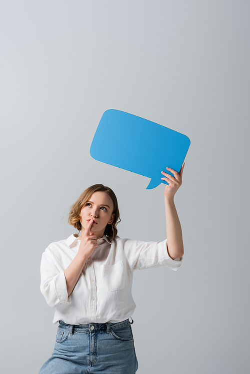 pensive overweight woman in white shirt holding blue speech bubble isolated on grey