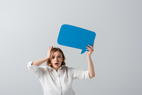 shocked overweight woman in white shirt holding blue speech bubble isolated on grey