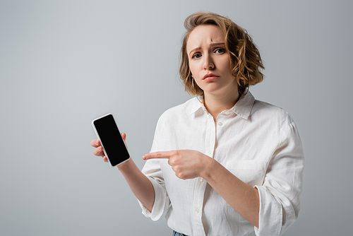 young overweight woman pointing at smartphone with blank screen isolated on grey