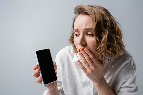 shocked overweight woman holding smartphone with blank screen isolated on grey