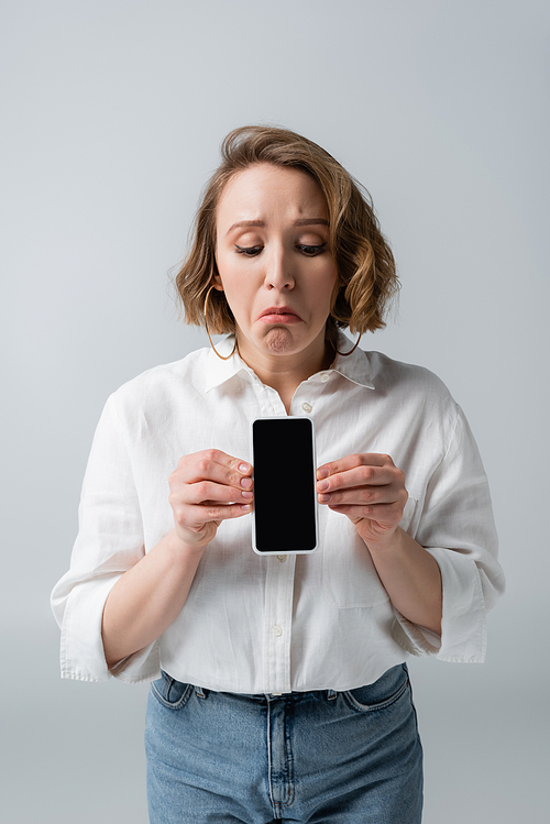 sad young overweight woman holding smartphone with blank screen isolated on grey