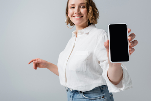 blurred young overweight woman holding smartphone with blank screen and smiling isolated on grey