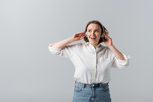 excited plus size woman in wireless headphones listening music isolated on grey