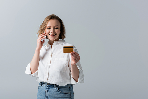 partial view of plus size woman holding credit card and talking on smartphone isolated on grey