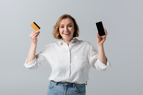 happy plus size woman holding credit card and smartphone isolated on grey