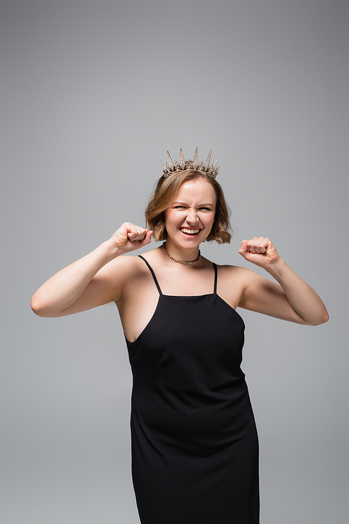 happy plus size woman in black slip dress and crown isolated on grey