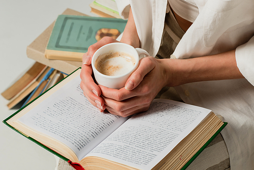 cropped view of woman with book holding cup of coffee isolated on white