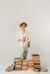 young woman in sun hat standing near pile of books isolated on white