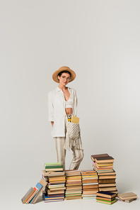 young woman in straw hat standing near pile of books isolated on white
