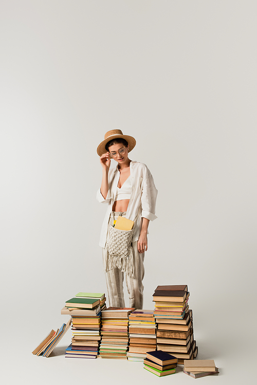 pretty young woman in sun hat standing near pile of books isolated on white