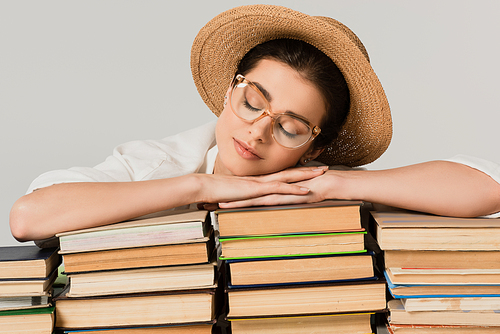 young woman in straw hat and glasses leaning on pile of books isolated on white