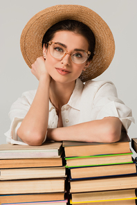 young woman in sun hat and glasses leaning on pile of books isolated on white