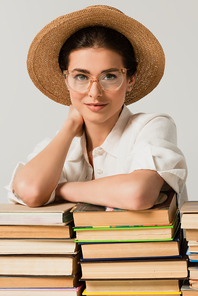 pleased woman in sun hat and glasses leaning on pile of books isolated on white