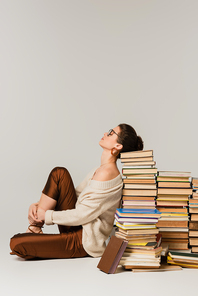 side view of young woman in glasses and sweater leaning on stack of books on white