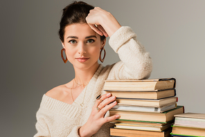 young woman in earrings leaning on stack of books on grey