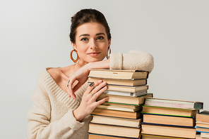 pleased young woman in earrings leaning on stack of books isolated on white