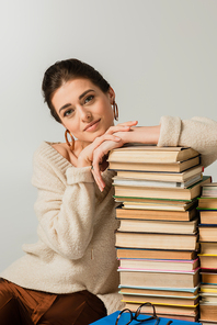 young woman in earrings leaning on stack of books isolated on white