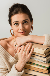 smiling young woman in earrings leaning on stack of books isolated on white