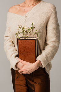 cropped view of young woman holding book with wildflowers isolated on grey