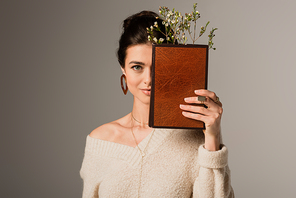young woman holding book in hardcover with flower isolated on grey