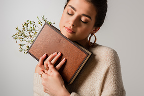 young woman with closed eyes holding book with wildflowers isolated on grey