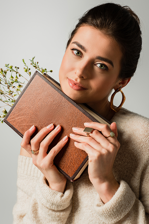 joyful young woman holding book with wildflowers isolated on grey
