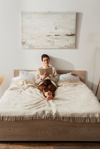 barefoot young woman reading book while resting on bed at home