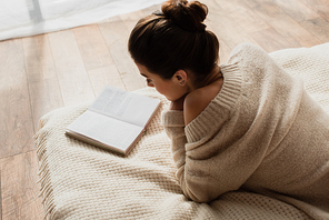 young woman reading novel while resting on bed at home