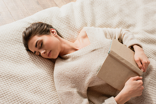 top view of young woman sleeping with book on bed