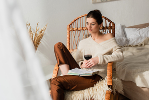 pretty young woman sitting in wicker rocking chair with book and glass of wine