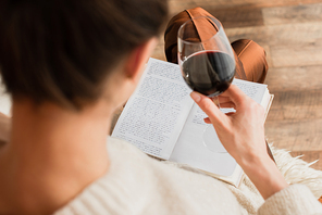 blurred young woman reading book and holding glass of red wine