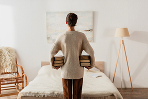 back view of woman holding stack of books in bedroom