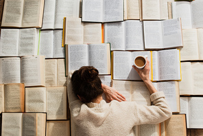 top view of tired woman sleeping near open books with cup of coffee