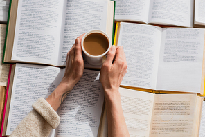 partial view of woman holding cup of coffee near open books